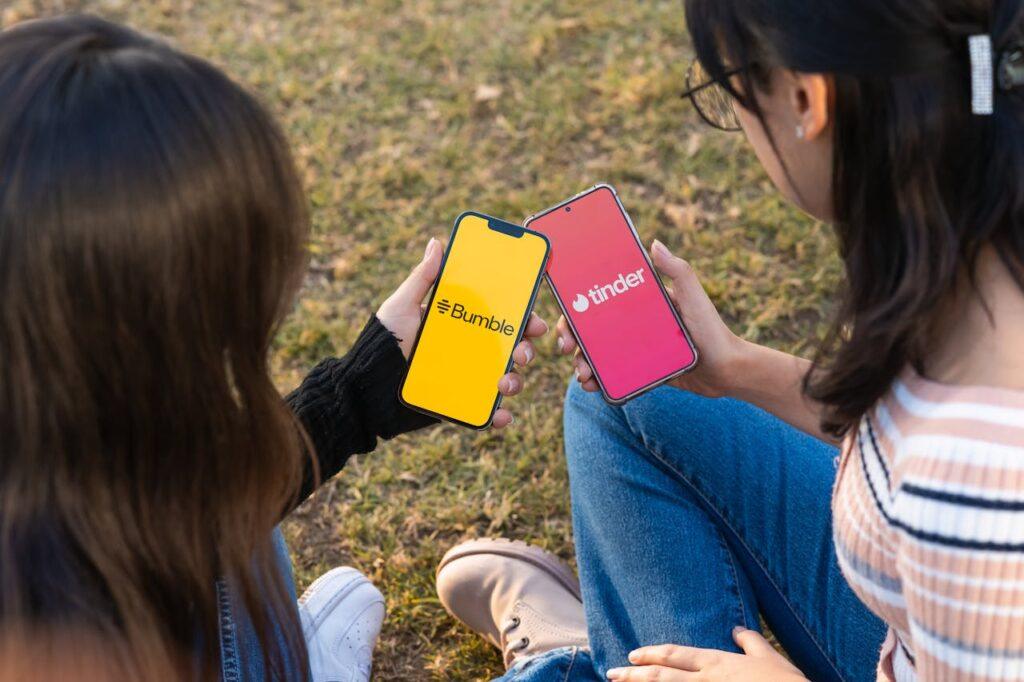 two young ladies holding their phones with screens showing dating apps