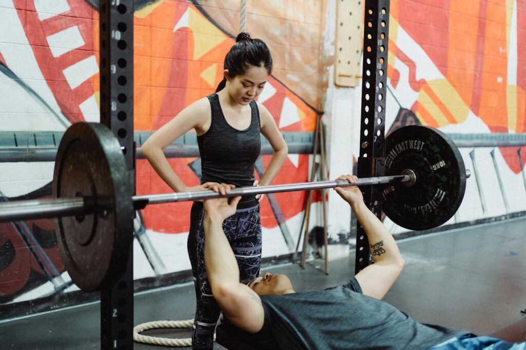 Weight lifting with a man on the bench press and a lady spotting for him.