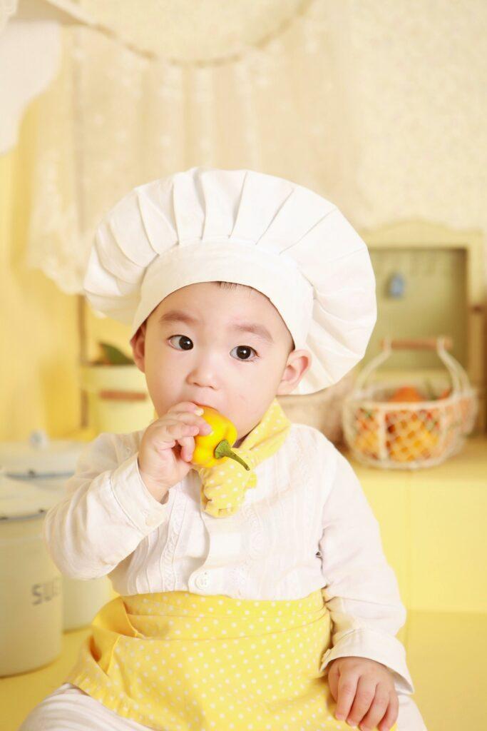 A young toddler dressed as a chef sitting on the kitchen counter